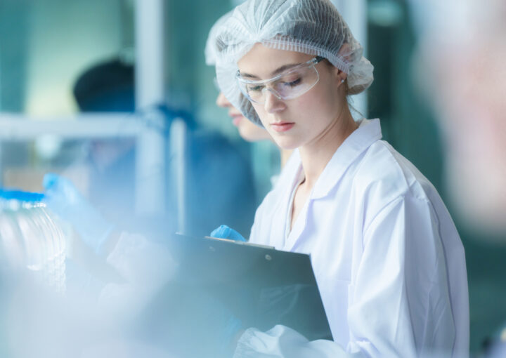scientist worker checking the quality of water bottles on the machine conveyor line at the industrial factory. Female worker recording data at the beverages manufacturing line production.